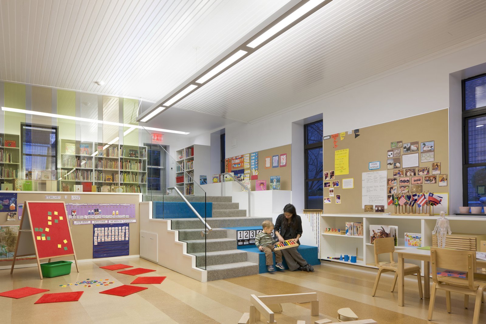 A nursery school classroom with tiered seating, bookshelves, and children’s learning materials.