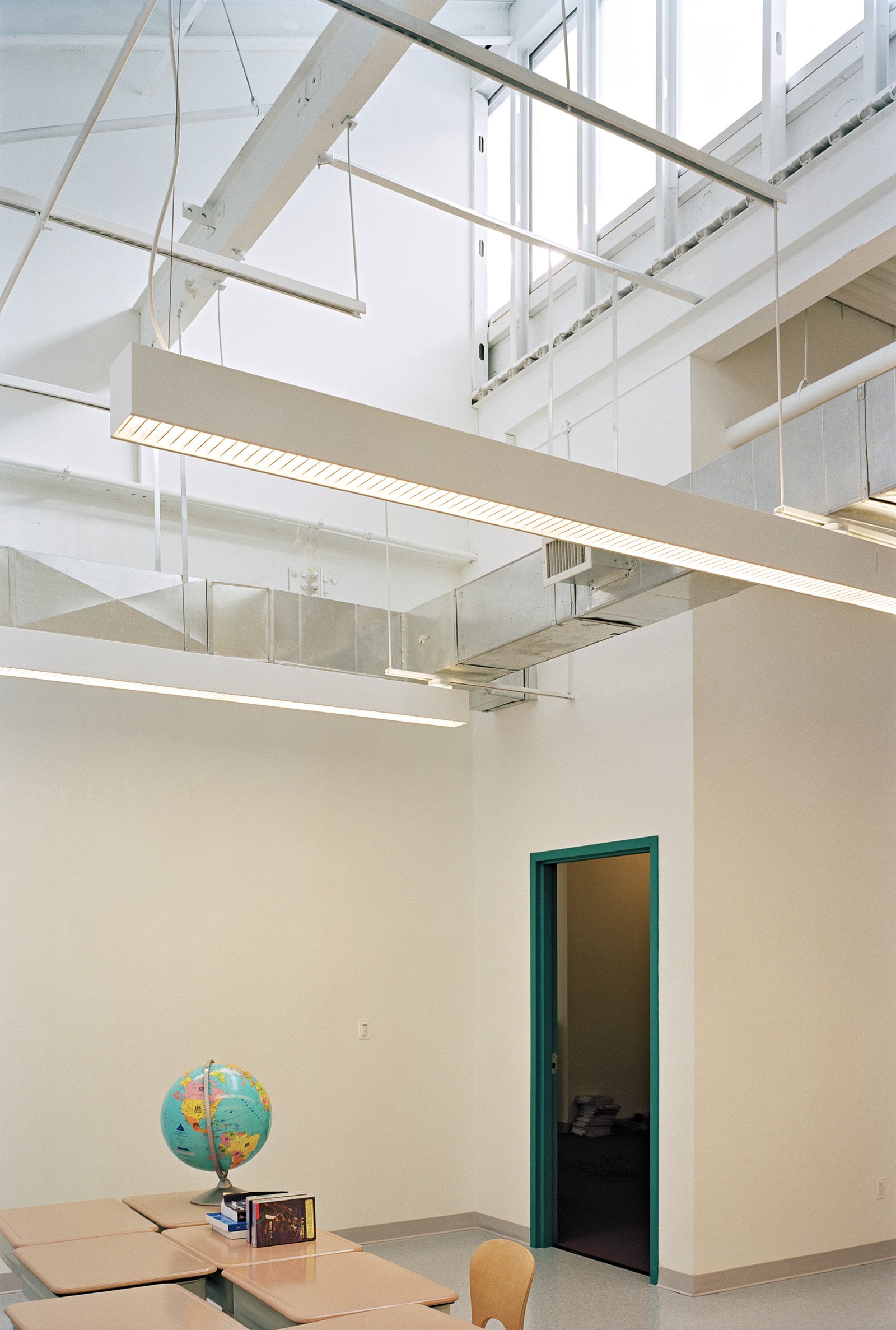 Minimalist classroom with high ceiling, exposed ductwork, and a globe on the table.