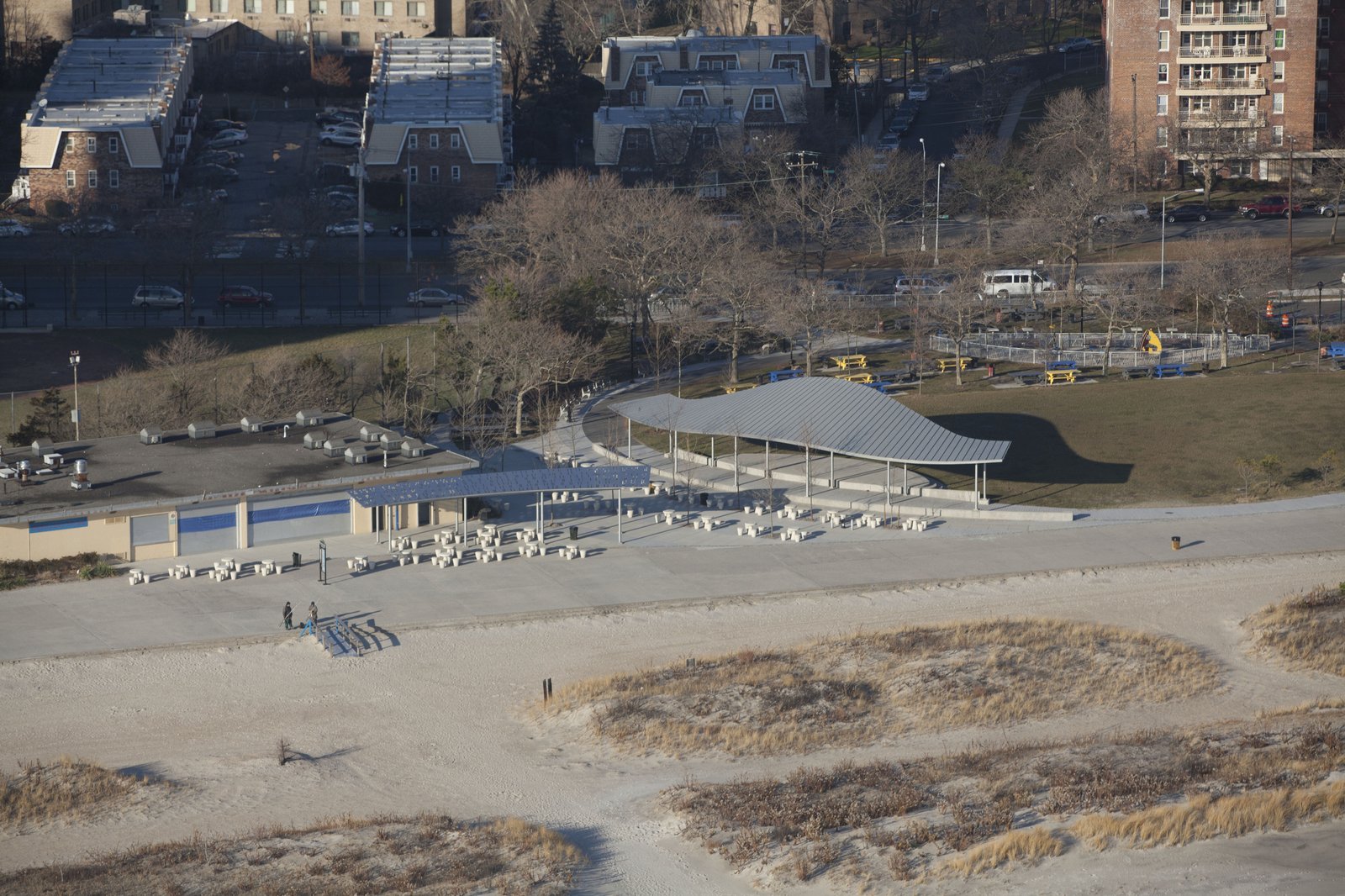 Aerial view of a park pavilion with a curved metal roof near a beach and open lawn.