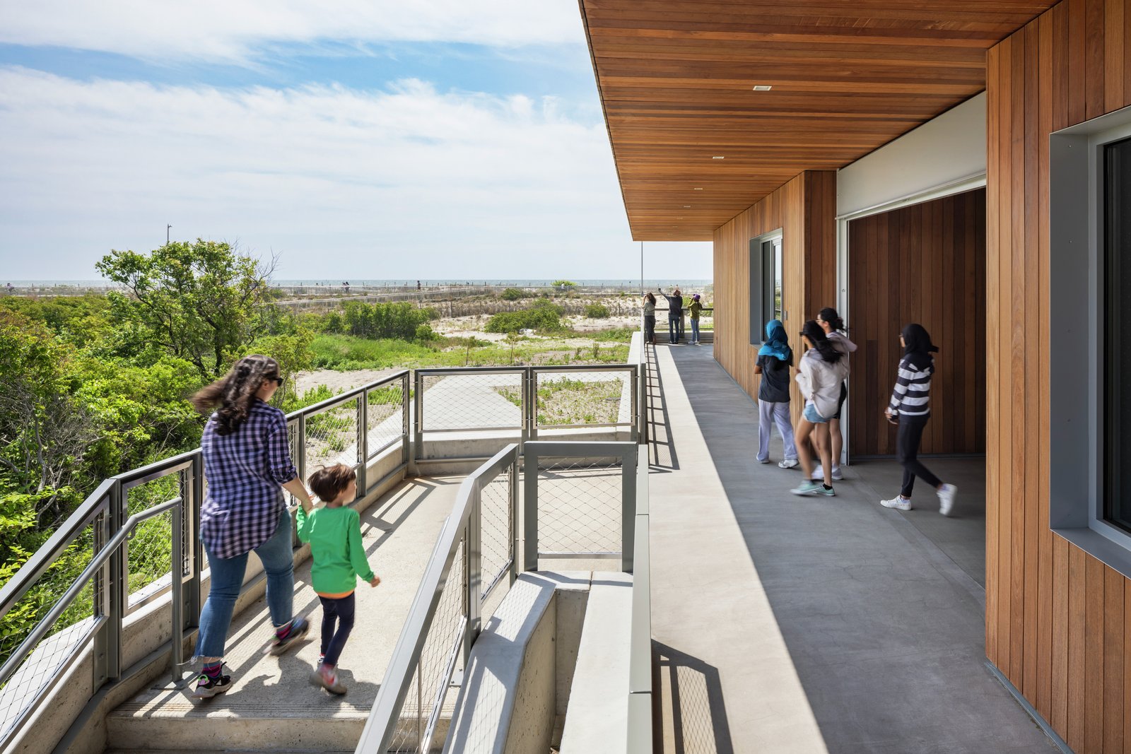 People walking along the Coastal Conservation Center wraparound porch with views of the ocean and surrounding greenery.