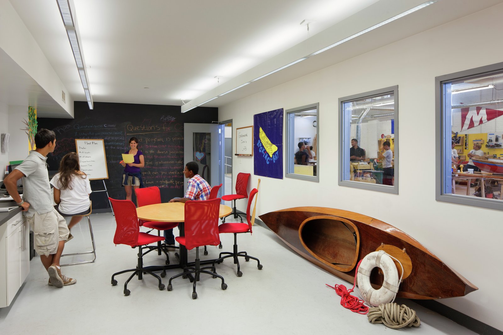 Classroom with students discussing near a chalkboard and a wooden boat.