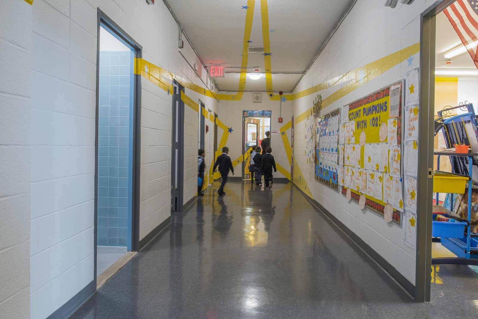 A school hallway with children walking, colorful wall graphics, and student artwork on display.