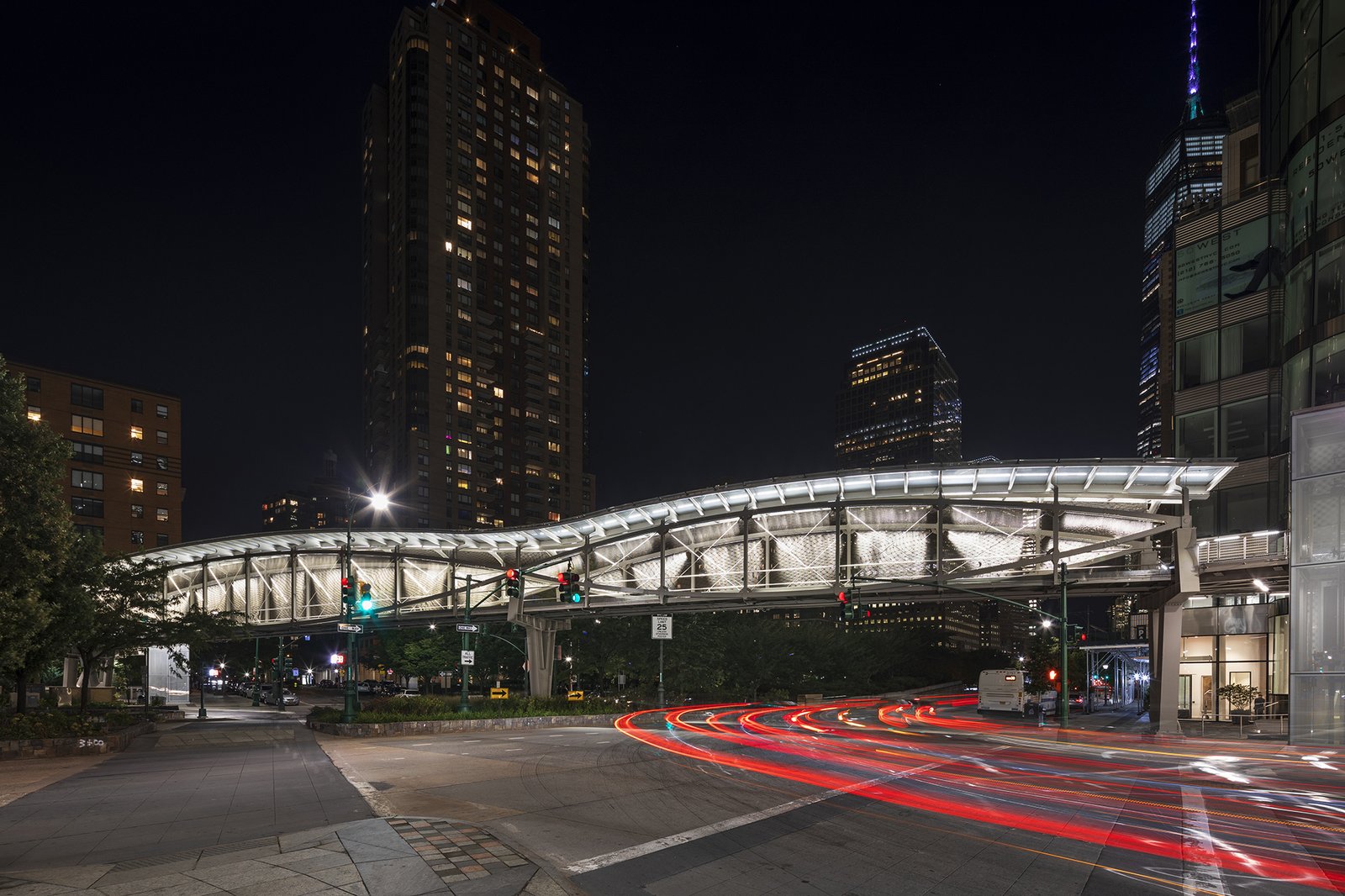 Illuminated pedestrian bridge at night with light trails from passing cars.