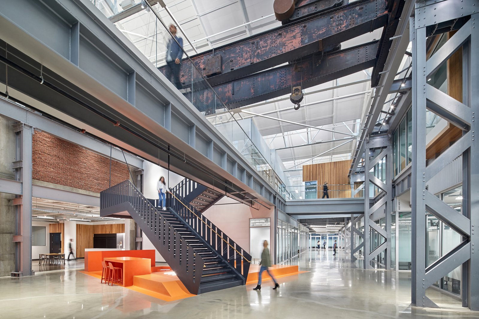 Industrial space featuring original crane beam, exposed brick, and new steel staircase with orange platform.