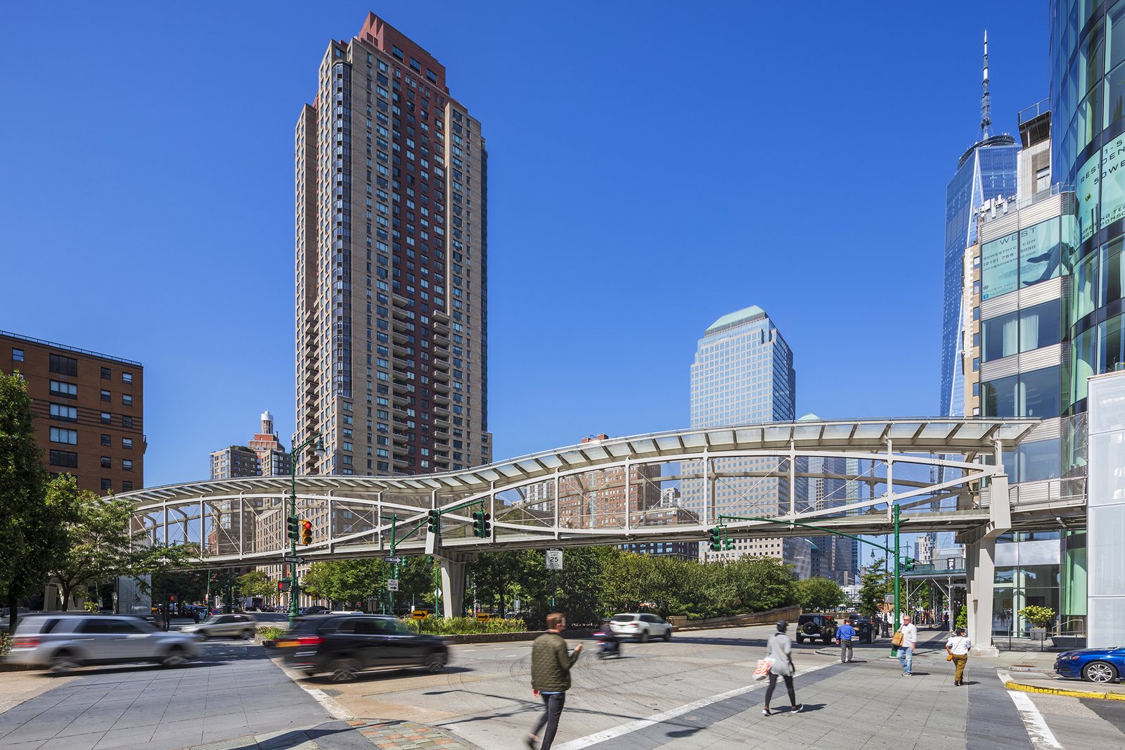 Pedestrian bridge in Lower Manhattan crossing over a busy city street with skyscrapers in view.