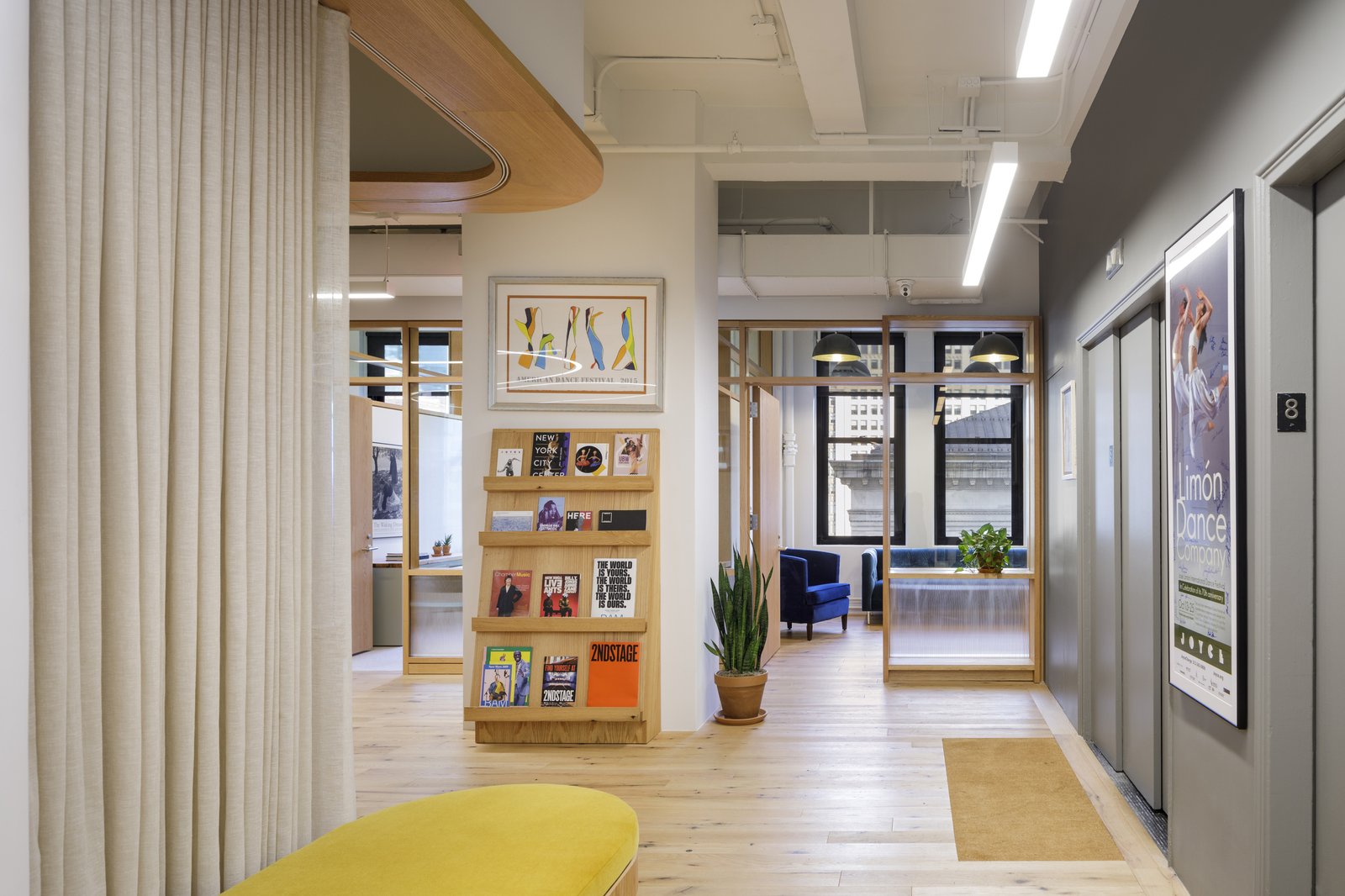 A bright office hallway with wood finishes, framed artwork, and plants.