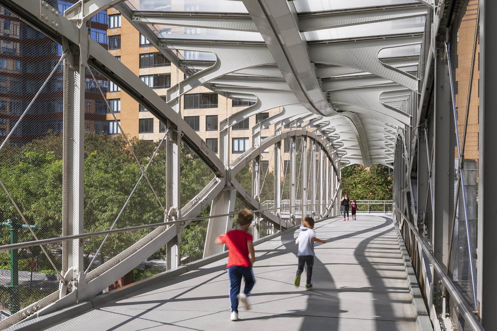 Children running across a covered pedestrian bridge with architectural truss details