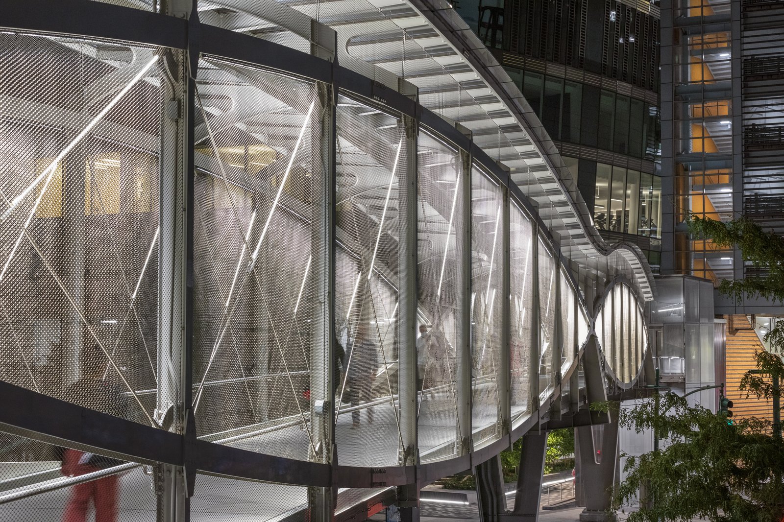 Night view of pedestrian bridge with metal mesh and integrated lighting.