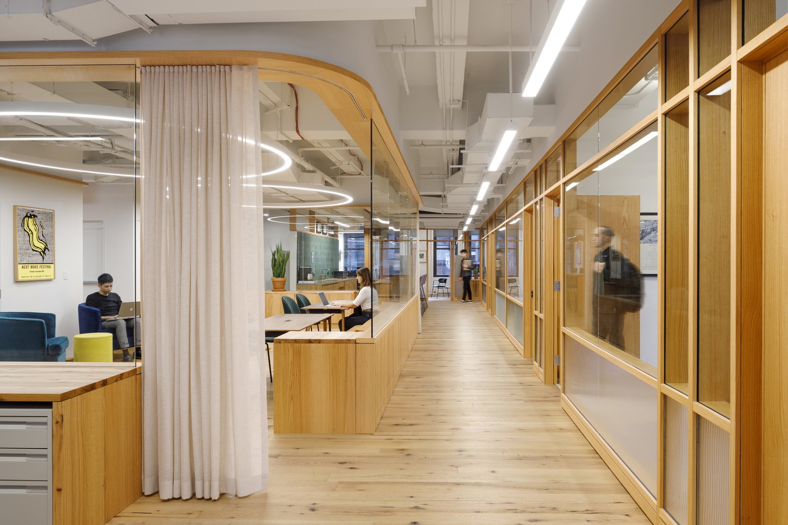 Open office hallway with wood finishes, glass partitions, and seating areas.