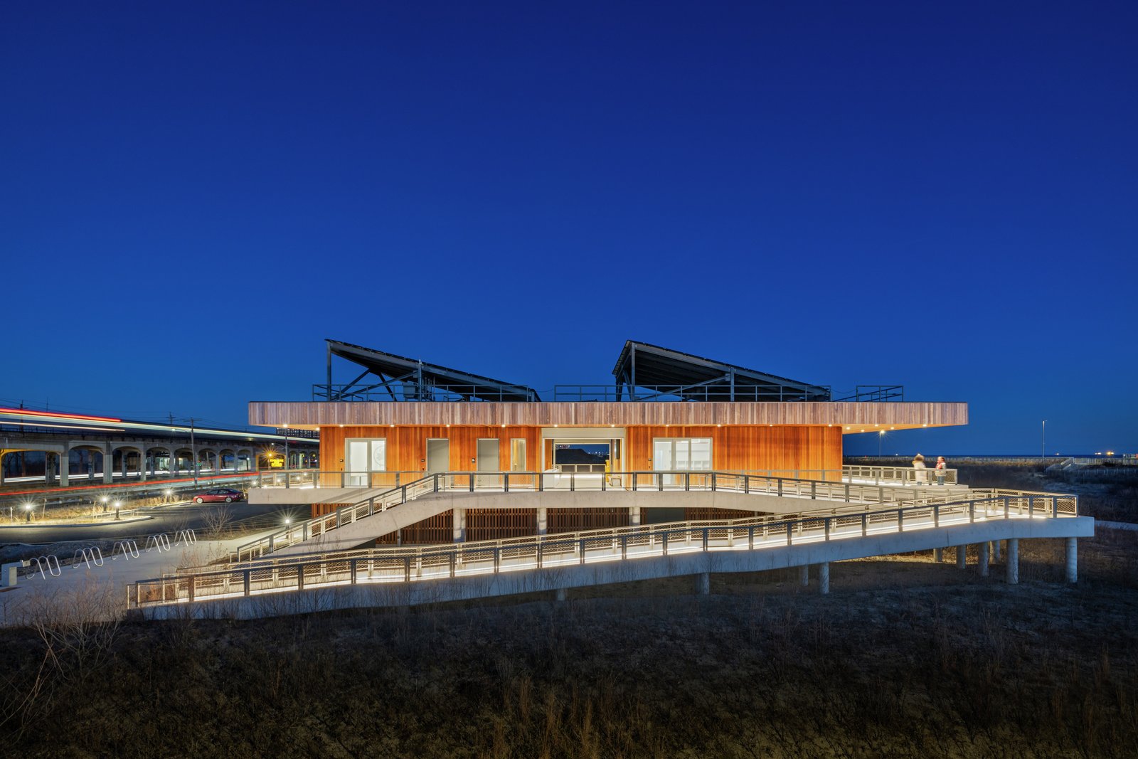 Night view of the Coastal Conservation Center with illuminated ramps and solar-paneled roof.