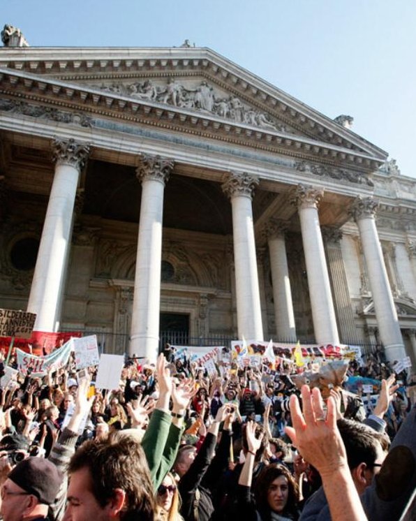 Crowd of protesters raising hands in front of a classical building with columns.