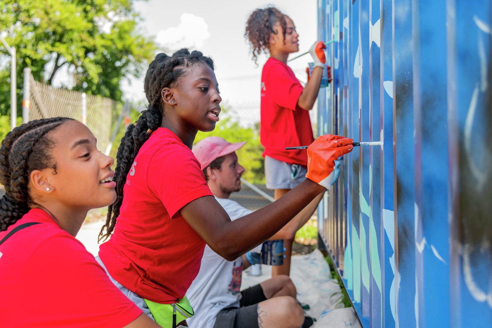 Young people paint a vibrant mural on a blue wall during a community engagement project.