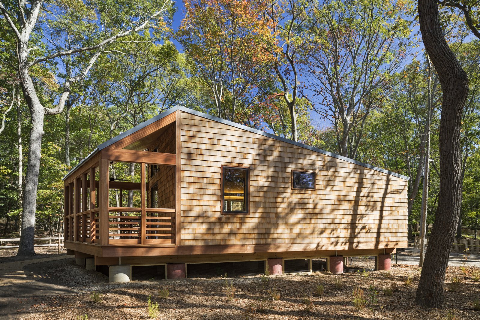 Wooden cabin with screened porch and cedar shingle exterior in a wooded area.