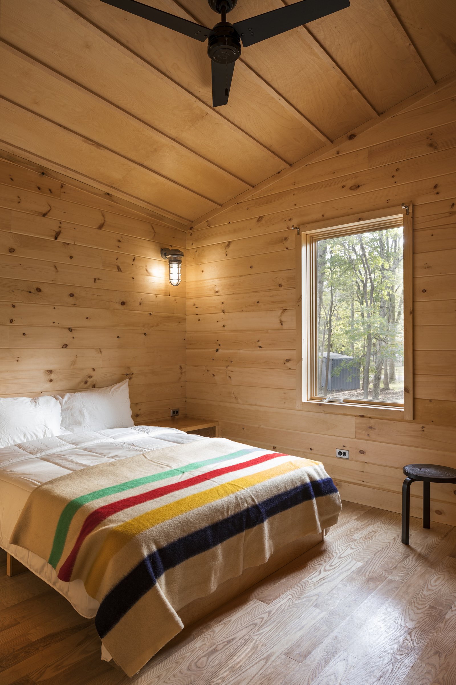 Cabin bedroom with natural wood walls, bed, and large window.