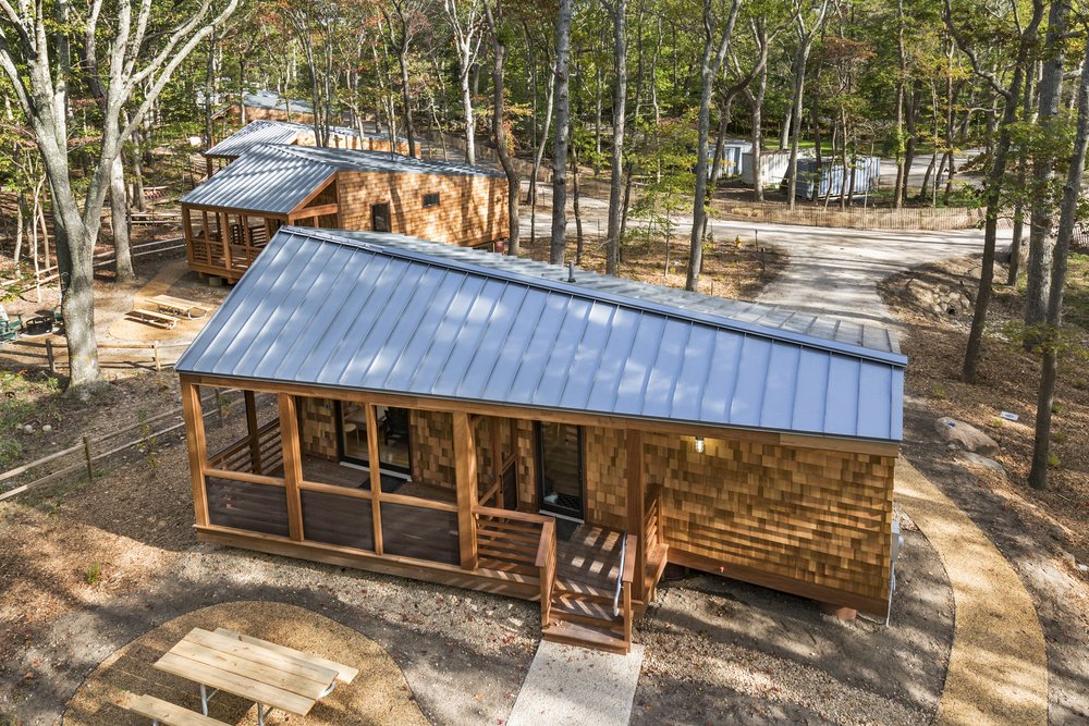 Cluster of wood-clad cabins with metal roofs nestled among trees.