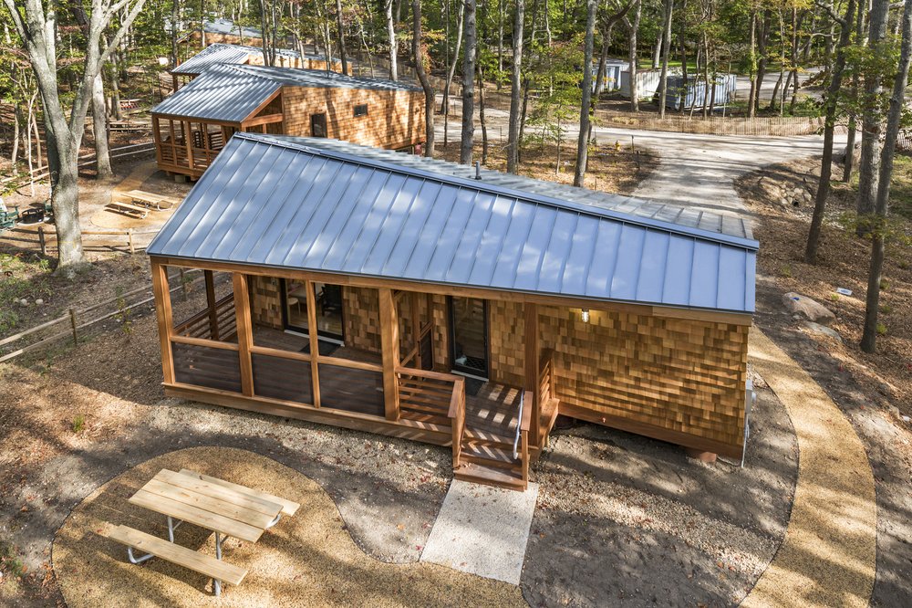 Cluster of wood-clad cabins with metal roofs nestled among trees.