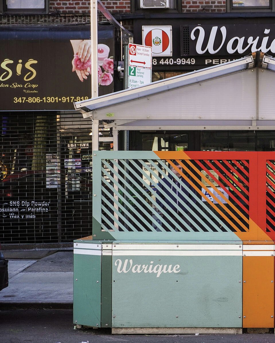 Colorful modular dining structure with diagonal slats and a pitched roof outside a restaurant.