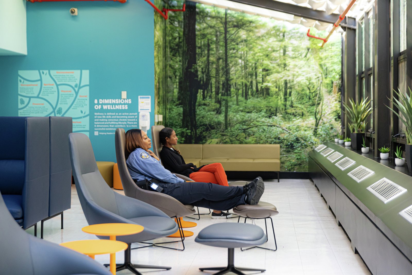 A serene wellness room with staff relaxing in ergonomic chairs, surrounded by lush forest murals and indoor plants.