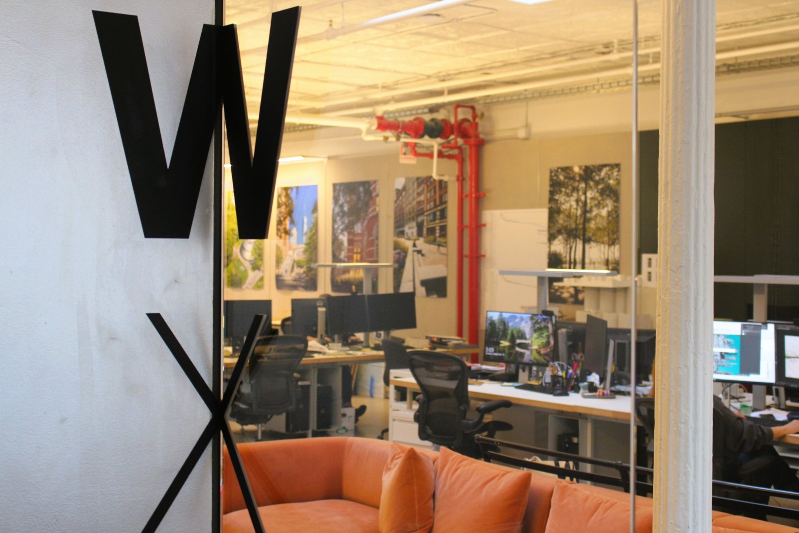 The entrance of the WXY Studio features the logo in the corner of the wall and and orange seating lounge.