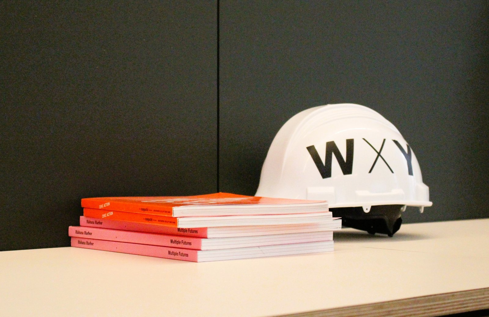 A stack of publications sits on a desk next to a hard hat with the WXY brand on it.